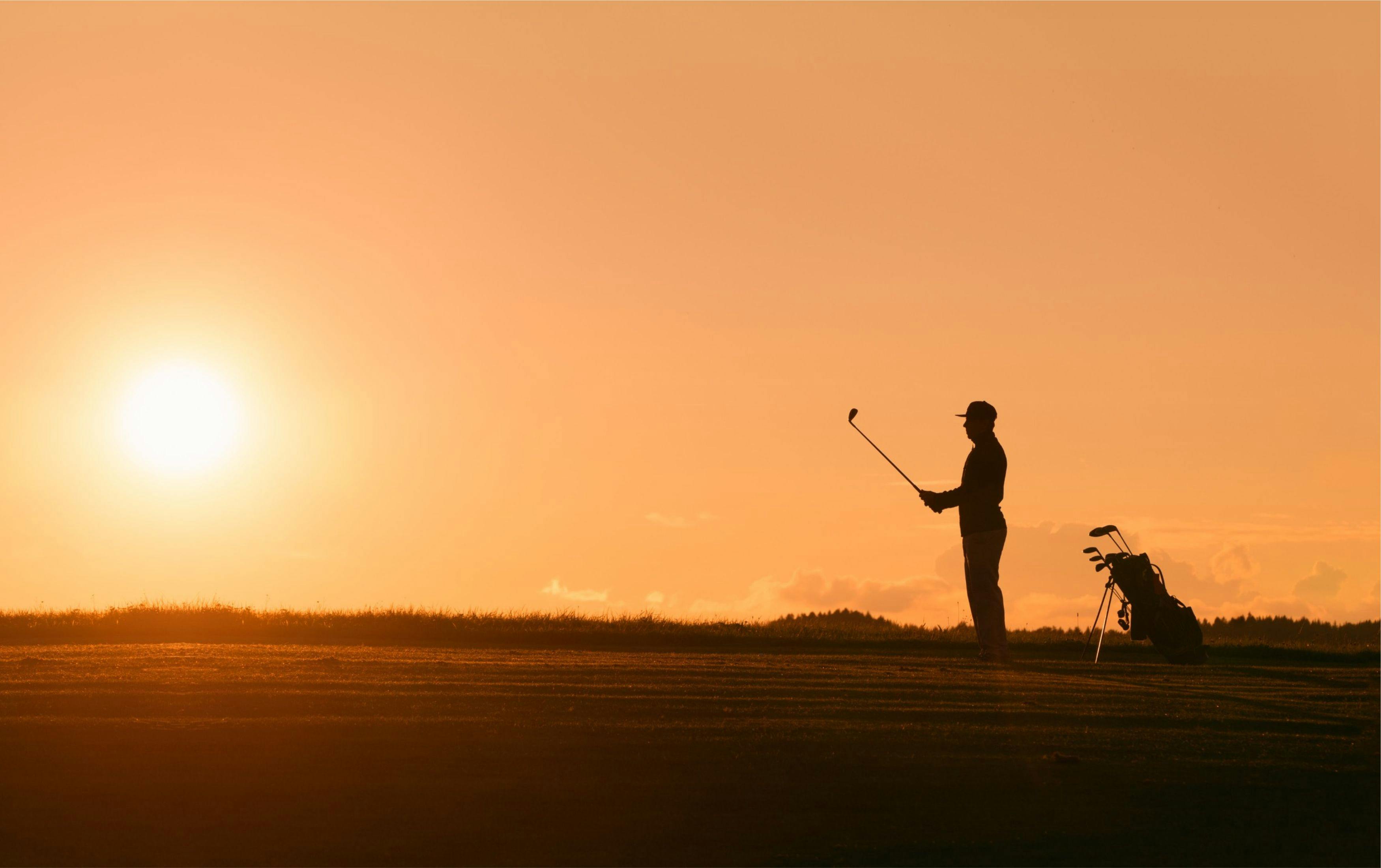 En golfspelare står vid horisonten under en målerisk solnedgång, redo för ett slag på den vackra golfbanan.